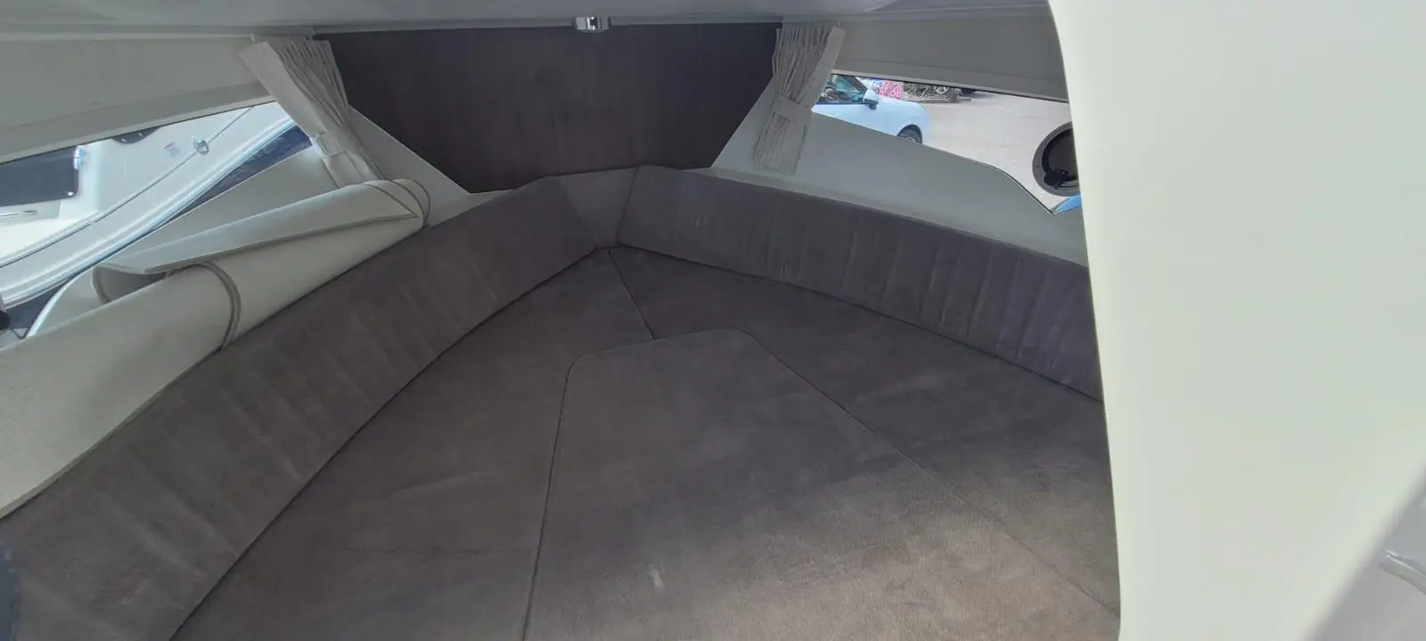 Cozy boat interior with curved seating and soft gray upholstery, featuring large windows and light curtains.